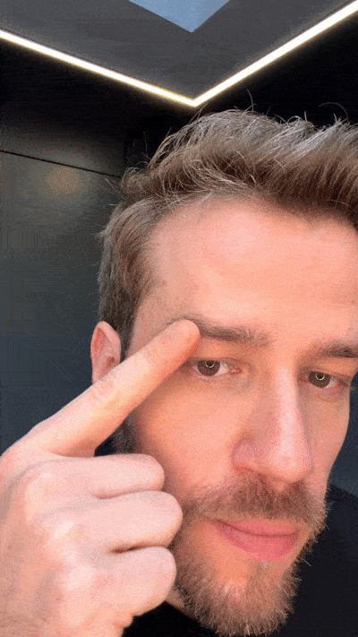 A gif showing a man applying the eyebrow growth serum to each eyebrow, rubbing it in with his fingertip, and smiling with the bottle.